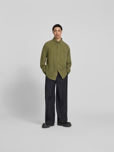 Männermodel trägt Freizeithemd aus reinem Lyocell von Filippa K in Oliv, Relaxed-Fit, Brusttasche, Button-Down-Kragen, Langärmelig, Ganzkörperansicht von vorne.