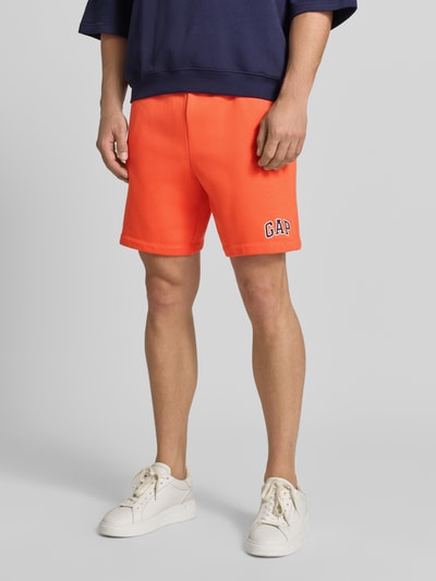 Mannelijk model draagt Straight fit korte broek met logostitching Model 'Heritage' van GAP, katoenmix, oranje, band met tunnelkoord, binnenbeenlengte 20 cm, bandwijdte maat M 40 cm, detailopname benen.