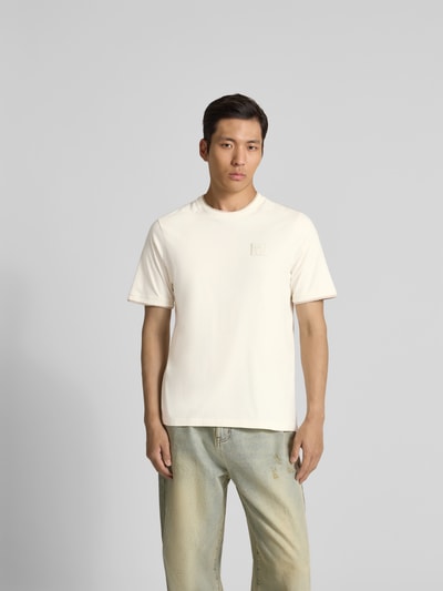 Männermodel trägt Slim Fit T-Shirt aus Baumwolle von MAISON KITSUNÉ in Creme mit Rundhalsausschnitt und Label-Detail, Ganzkörperansicht von vorne.