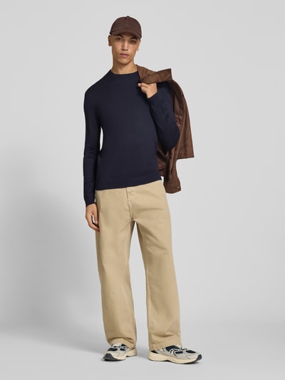Männermodel trägt dunkelblauen Regular Fit Pullover aus Viskose-Mix Modell 'WYLER' von ONLY & SONS, helle Hose, Sneakers, Ganzkörperansicht von vorne.