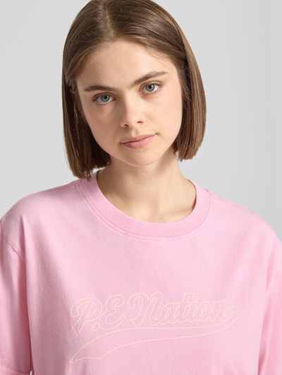 Frauenmodel trägt Damen T-Shirt von P.E Nation in Rosa aus Reine Baumwolle, Relaxed-Fit, Modell 'Formation' mit Logo-Print, Rundhalsausschnitt, Nahaufnahme Oberkörper.