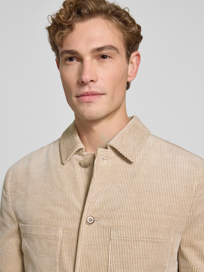 Męski model nosi Slim Fit Hemdjacke aus Cord von MCNEAL, mieszanka bawełny i elastanu, jasny sztruks, kieszenie na piersi, kołnierzyk typu kent, listwa guzikowa, długość tyłu w rozmiarze M: 70 cm, zbliżenie na górną część ciała.
