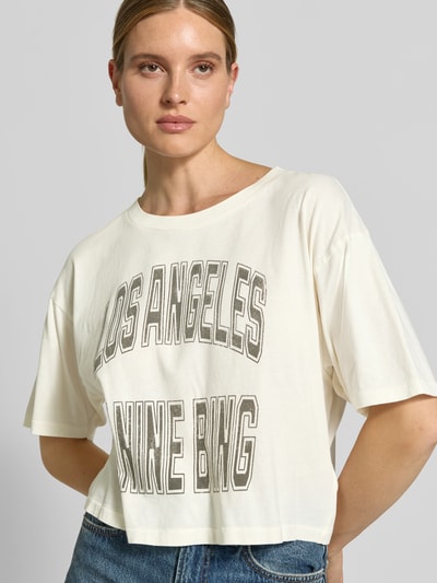 Vrouwenmodel draagt Cropped T-Shirt met Labelprint van Anine Bing in crème, puur katoen, kort, losse pasvorm, ruglengte maat S 42 cm, Nahaufnahme Oberkörper