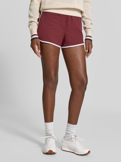 Frauenmodel trägt Regular Fit Shorts mit elastischem Bund Modell 'Marty' von VARLEY, bordeaux mit weißen Details, Damen Shorts im elastischen Material-Mix, Bundweite 35 cm, Innenbeinlänge 6 cm, Nahaufnahme Oberkörper bis Knie