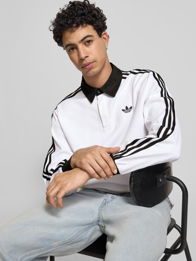 Männermodel trägt Regular Fit Longsleeve mit Logo-Stitching von adidas Originals in Weiß mit schwarzen Details, Nahaufnahme Oberkörper.