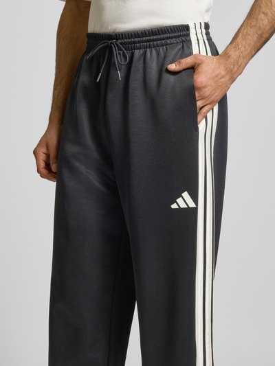 Männermodel trägt Sweatpants mit elastischem Bund von adidas Sportswear in Dunkelgrau mit Label-Print, Material-Mix, Eingrifftaschen, Nahaufnahme Oberkörper.