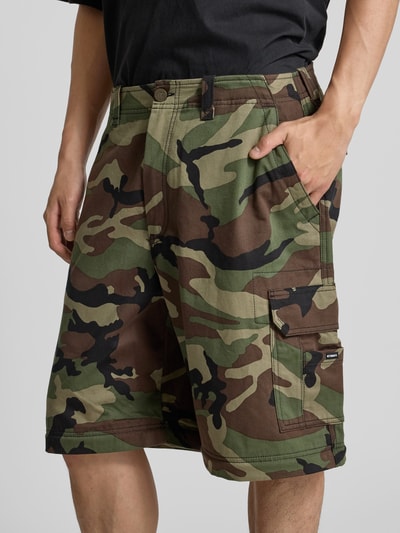 Männermodel trägt Relaxed Fit Cargohose aus Baumwolle von VETEMENTS, Camouflage-Muster, Cargotaschen, Nahaufnahme Oberschenkel.
