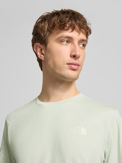 Męski model nosi T-shirt mit Label-Print od The North Face, mieszanka bawełny, krój regular fit, okrągły dekolt, nadruk z logo, jasny kolor, gładka faktura. Nahaufnahme oberkörper. Długość tyłu w rozmiarze M: 71 cm.