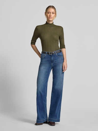 Frauenmodel trägt Slim Fit Longsleeve aus reiner Lanawolle Modell 'Maglia Costine' von Liu Jo White in Olivgrün, semitransparent, gerippte Struktur, Stehkragen, Halbarm, kombiniert mit blauen Jeans, Ganzkörperansicht von vorne.