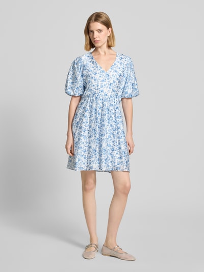 Frauenmodel trägt Freizeitkleid von Vero Moda, Modell 'BLISS', Optik:Allover-Muster, Passform: Tailliert, Mini-Länge, V-Ausschnitt, Ärmelform: Ballonärmel, gerader Saum, Materialverarbeitung: feine Webstruktur, Viskose-Mix, Farbgebung in Hellblau und Weiß, Ganzkörperansicht von vorne.