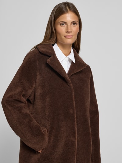 Frauenmodel trägt Wendemantel in Woll-Lammfell-Optik Modell 'VENUS' von OAKWOOD, braun, lockere Passform, Nahaufnahme Oberkörper.