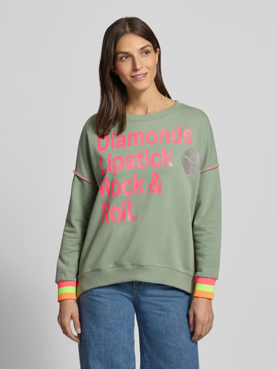 Modelka nosi Oversized Sweatshirt mit gerippten Abschlüssen von miss goodlife z bawełny, krój oversized, prążkowane wykończenia, okrągły dekolt, nadruk z napisem, widok całej sylwetki z przodu.