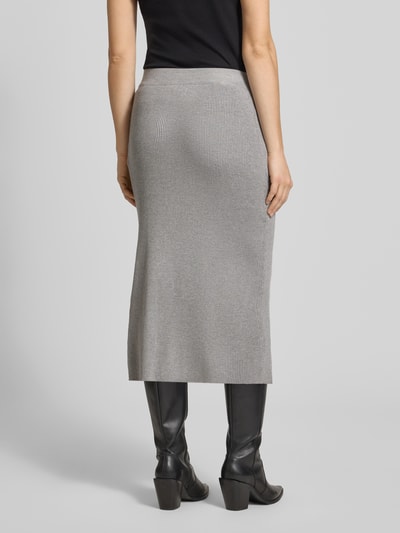 Modelka nosi Strickrock mit Label-Patch und elastischem Bund von Karo Kauer, mieszanka wiskozy, dopasowany krój, spódnica midi, drobne prążkowanie, naszywka z logo, elastyczny pas, kolor szary, szerokość w rozmiarze S 37 cm, całkowita długość 80 cm, widok całej sylwetki z tyłu.