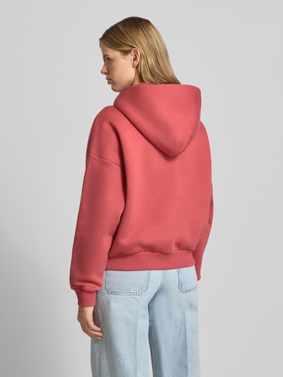 Frauenmodel trägt Relaxed Fit Sweatjacke mit Kapuze und Logo-Print von REVIEW aus Baumwoll-Mix in Rosa, Känguru-Tasche, Rückenansicht.