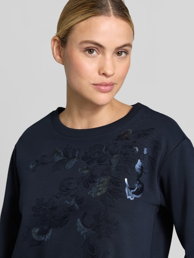 Frauenmodel trägt Regular Fit Longsleeve aus Baumwoll-Mix mit Spitzenbesatz von Milano Italy, florales Design, Pailettenbesatz, Rundhalsausschnitt, dunkle Farbe, Nahaufnahme Oberkörper.