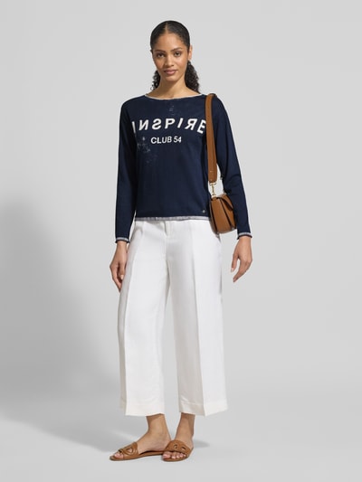 Frauenmodel trägt Longsleeve mit Linksdruck und Rundhalsausschnitt von monari in Dunkelblau, weiße Hose, braune Tasche, Regular Fit aus reiner Baumwolle, Rückenlänge 55 cm, Ganzkörperansicht von vorne.