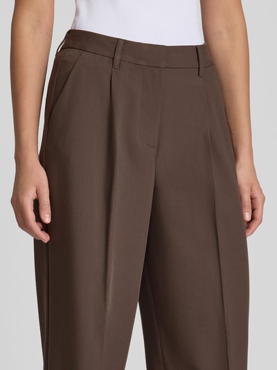 Frauenmodel trägt Wide Fit Hose mit Viskose-Anteil Modell 'Aya Ellis' von JJXX in Braun mit Bund- und Bügelfalten, Nahaufnahme Oberkörper. Damen Hose von JJXX, elastischer Material-Mix, Haken- und Reißverschluss, Bundweite 37 cm, Innenbeinlänge 77 cm.