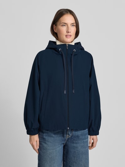 Frauenmodel trägt Relaxed Fit Regenjacke mit Baumwoll-Anteil Modell 'ROMANA' von Weekend Max Mara, unifarben dunkelblau, Kapuze mit Tunnelzug, Logo-Patch, elastische Ärmelabschlüsse, seitliche Eingrifftaschen, wasserabweisend, Ganzkörperansicht von vorne.