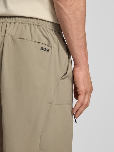 Männermodel draagt Relaxed Fit Cargoshorts met label-schrift 'GLOBE CARGO' van BOSS Green, uni, elastische tailleband, detailopname heup.
