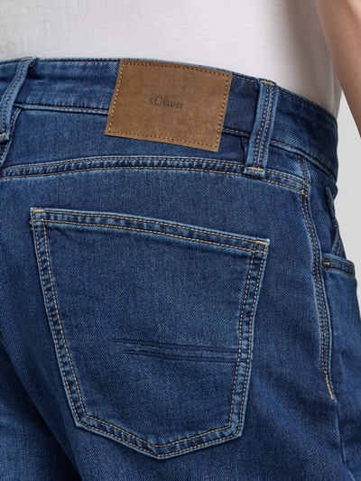 Männermodel trägt Regular Fit Jeansshorts aus Baumwoll-Mix von s.Oliver RED LABEL in blauer Denim-Optik mit Label-Patch, Nahaufnahme Rückansicht. 5-Pocket-Design, Nieten, markante Nähte, robuste Textur, Passform: Regular-Fit.