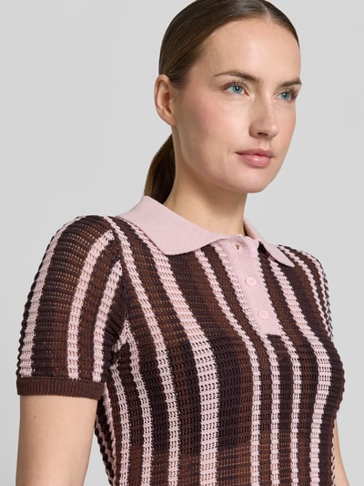 Frauenmodel trägt Modern Fit Poloshirt in Strick-Optik Modell 'PETRA' von Mango aus Baumwoll-Mix mit Polokragen, Nahaufnahme Oberkörper. Rückenlänge bei Größe S: 53 cm, Ärmellänge bei Größe S: 23 cm, kurze Knopfleiste, Streifen in Braun und Rosa, strukturierte Textur.