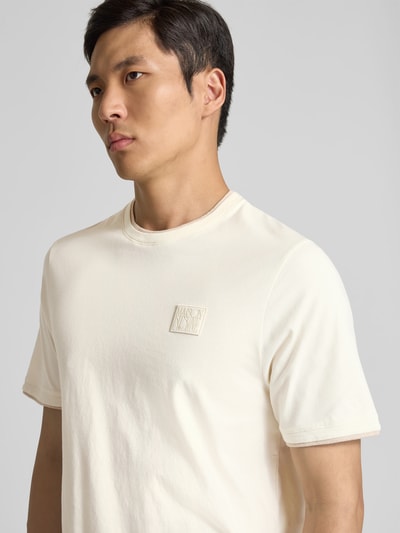 Männermodel trägt Slim Fit T-Shirt aus Baumwolle von MAISON KITSUNÉ in Creme mit Rundhalsausschnitt, Label-Detail, Nahaufnahme Oberkörper.