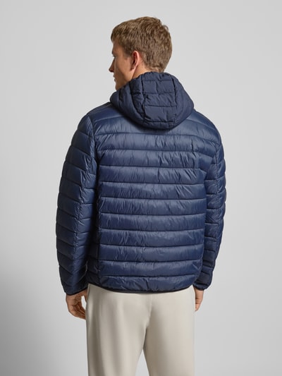 Männermodel draagt Steppjacke mit Kapuze und Logo van CHAMPION in donkerblauw, regular fit, horizontale stiksels, Ganzkörperansicht Rückansicht.