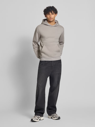 Männermodel trägt Hoodie mit Känguru-Tasche von REVIEW in Grau, lockere Passform, Baumwollmischung, Ganzkörperansicht von vorne.
