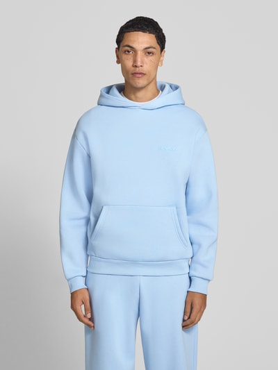 Männermodel trägt Hoodie mit Logo-Print von REVIEW in Hellblau, lockere Passform, Baumwoll-Mix, Kängurutasche, Ganzkörperansicht von vorne.