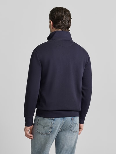 Mężczyzna nosi Regular Fit Sweatjacke mit Stehkragen Modell 'Gield' od Gant, bawełniany miks, granatowy, z logo, suwak, elastyczne wykończenia, widok całej sylwetki od tyłu.