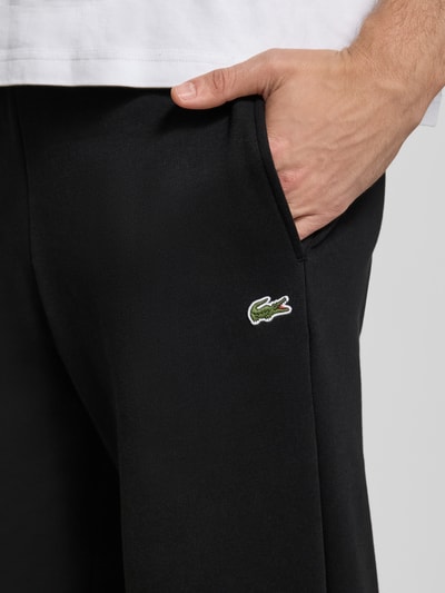 Männermodel draagt Sweatpants mit Label-Detail van Lacoste in effen zwart katoenmix met zij-steekzakken, recht model, detailopname.