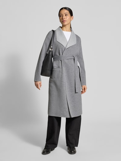Modelka nosi Relaxed Fit Mantel mit Viskose-Anteil Modell 'Juice' od Vila, szary, pasek, kieszenie, długość 95 cm, krój relaxed fit, widok całej sylwetki z przodu.