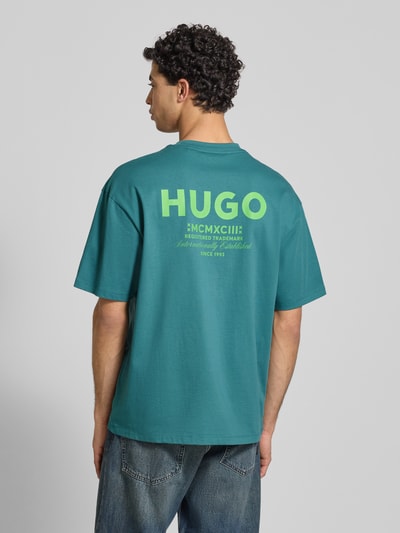 Männermodel trägt Oversized T-Shirt aus reiner Baumwolle Modell 'NALONO' von Hugo Blue in Unifarbe mit Label Print, Ganzkörperansicht Rückansicht.