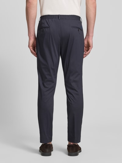 Männermodel trägt Regular Fit Stoffhose mit Logo-Detail Modell 'Lester' von JOOP! Collection aus dunkelblauem Baumwoll-Mix mit Bundfalten, Gesäßtaschen und Knopf-Reißverschluss, Ganzkörperansicht Rückansicht.