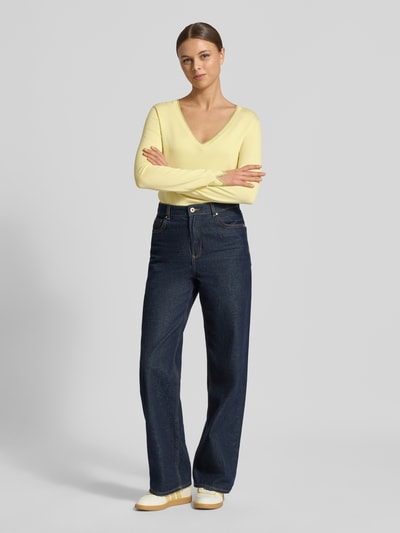 Frauenmodel trägt Slim Fit Longsleeve aus Viskose-Mix mit V-Ausschnitt von Liu Jo White in Gelb, kombiniert mit dunkler Jeans, Logo-Detail, elastische Abschlüsse, Rückenlänge 55 cm, Ärmellänge 58 cm, Ganzkörperansicht von vorne.