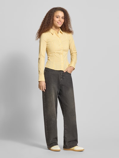 Modelka nosi Fitted Hemdbluse mit Hemdblusenkragen od Review, elastyczna mieszanka bawełny, krój fitted, długi rękaw, żółte paski, widok całej sylwetki z przodu.