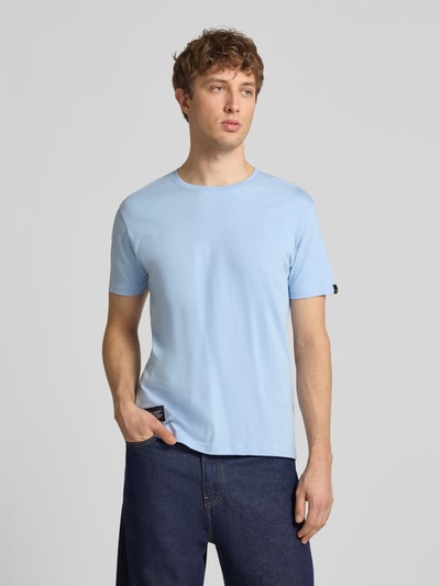 Męski model nosi T-Shirt mit Label-Patch od Alpha Industries z bawełny, prosty krój, okrągły dekolt, jasnoniebieski, widok z przodu, długość tyłu w rozmiarze M: 66 cm.