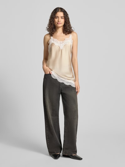 Frauenmodel trägt Slim Fit Trägertop mit Spitzenbesatz Modell 'JESSA' von PIECES, Optik: Unifarben, Passform: Slim-Fit, Applikation: Spitzenbesatz, Ausschnitt: V-Ausschnitt, Trägerform: Verstellbare Spaghettiträger, Rumpfabschluss: Asymmetrisch mit Satin, in Beige und Weiß, sanfte Haptik, Ganzkörperansicht von vorne.