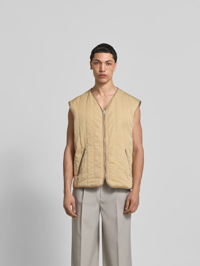 Männermodel trägt Relaxed Fit Weste in Stepp-Optik von MM6 Maison Margiela, beige, mit Reißverschluss, Eingrifftaschen, Ganzkörperansicht von vorne.