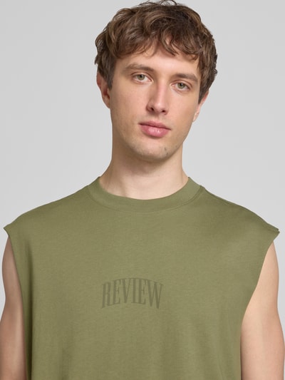 Männermodel trägt Muskelshirt mit Logo und Rundhalsausschnitt von REVIEW in Olivgrün aus reiner Baumwolle, Regular Fit, Nahaufnahme Oberkörper.