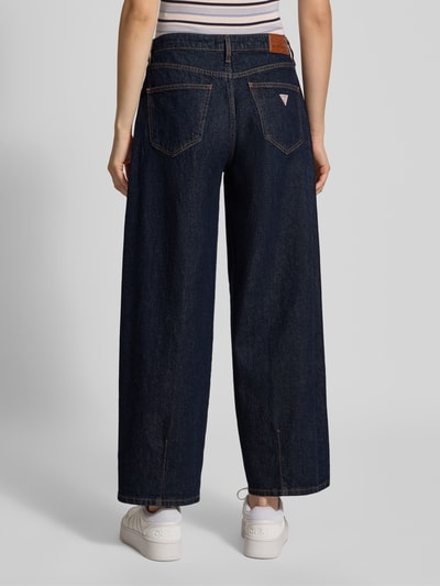 Frauenmodel trägt Barrel Fit Jeans in verkürzter Passform von GUESS, dunkelblau, 5-Pocket-Design, Rückansicht, Ganzkörperansicht.