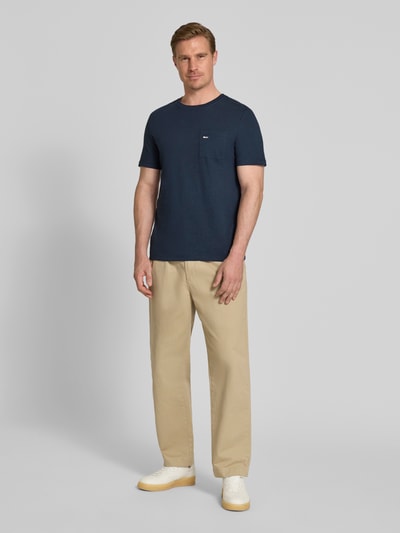 Męski model nosi Regular Fit T-Shirt aus reiner Baumwolle od s.Oliver RED LABEL, granatowy melanż, krój regular fit, łatka z logo, okrągły dekolt, krótki rękaw, kieszonka na piersi, bawełna, widok całej sylwetki z przodu.