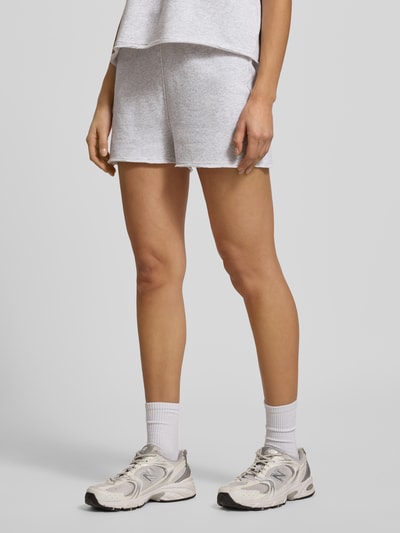 Kobiece modelka nosi Sweatshorts mit elastischem Bund Modell 'TUBAY' od American Vintage, jasnoszary kolor, bawełna z domieszką elastanu, prosty krój, kieszeń z tyłu, kieszenie boczne, długość nogawki 9 cm w rozmiarze S; całkowity widok od przodu.