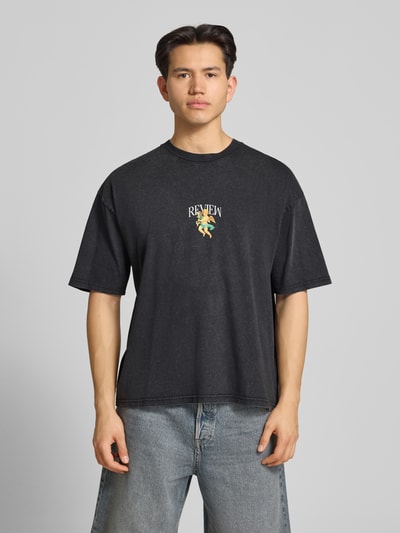 Männermodel trägt T-Shirt mit überschnittenen Schultern von REVIEW, reine Baumwolle, lockerer Schnitt, dunkle Farbe, Ganzkörperansicht von vorne