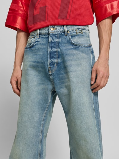 Männermodel trägt Wide Fit Jeans im 5-Pocket-Design von RHUDE aus Material-Mix mit Baumwoll-Anteil, Zierbesatz, Knopf- und Reißverschluss, Nahaufnahme Oberkörper.