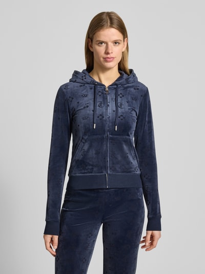 Kobiece model prezentuje bluzę rozpinaną z kapturem Model 'MONO MADISON' od Juicy Couture, mieszanka materiałów z dodatkiem streczu, krój slim fit, kaptur z tunelem, zamek błyskawiczny, kieszeń kangurka, ciemnoniebieska, faktura welurowa. Ganzkörperansicht von vorne.