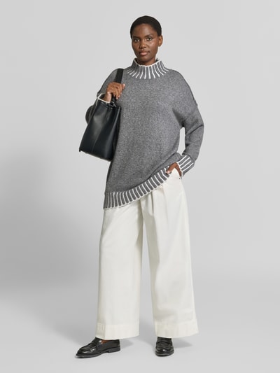 Kobieta nosi sweter z dzianiny 'Strickpullover mit Stehkragen und überschnittenen Schultern' od Apricot, krój relaxed fit, Dwa kolory, stójka, wydłużony tył 79 cm, długość rękawów 49 cm; jasnoszare i białe detale, luźna faktura, Ganzkörperansicht von vorne