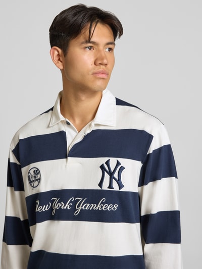 Männermodel trägt Relaxed Fit Poloshirt aus reiner Baumwolle von Champion, navy-weiße Blockstreifen, Statement-Stitching, Nahaufnahme Oberkörper.