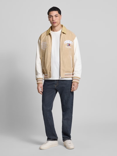 Männermodel trägt Relaxed Fit College-Jacke aus echtem Leder von Tommy Jeans in Lederoptik, naturweiß-beige, Ganzkörperansicht von vorne.