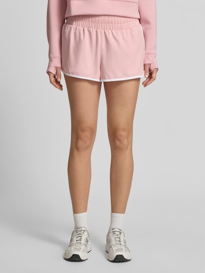 Frauenmodel trägt Running Shorts mit elastischem Bund von VARLEY in Rosa mit weißem Rand, entspannter Schnitt, Material-Mix mit Stretch, Ganzkörperansicht von vorne.